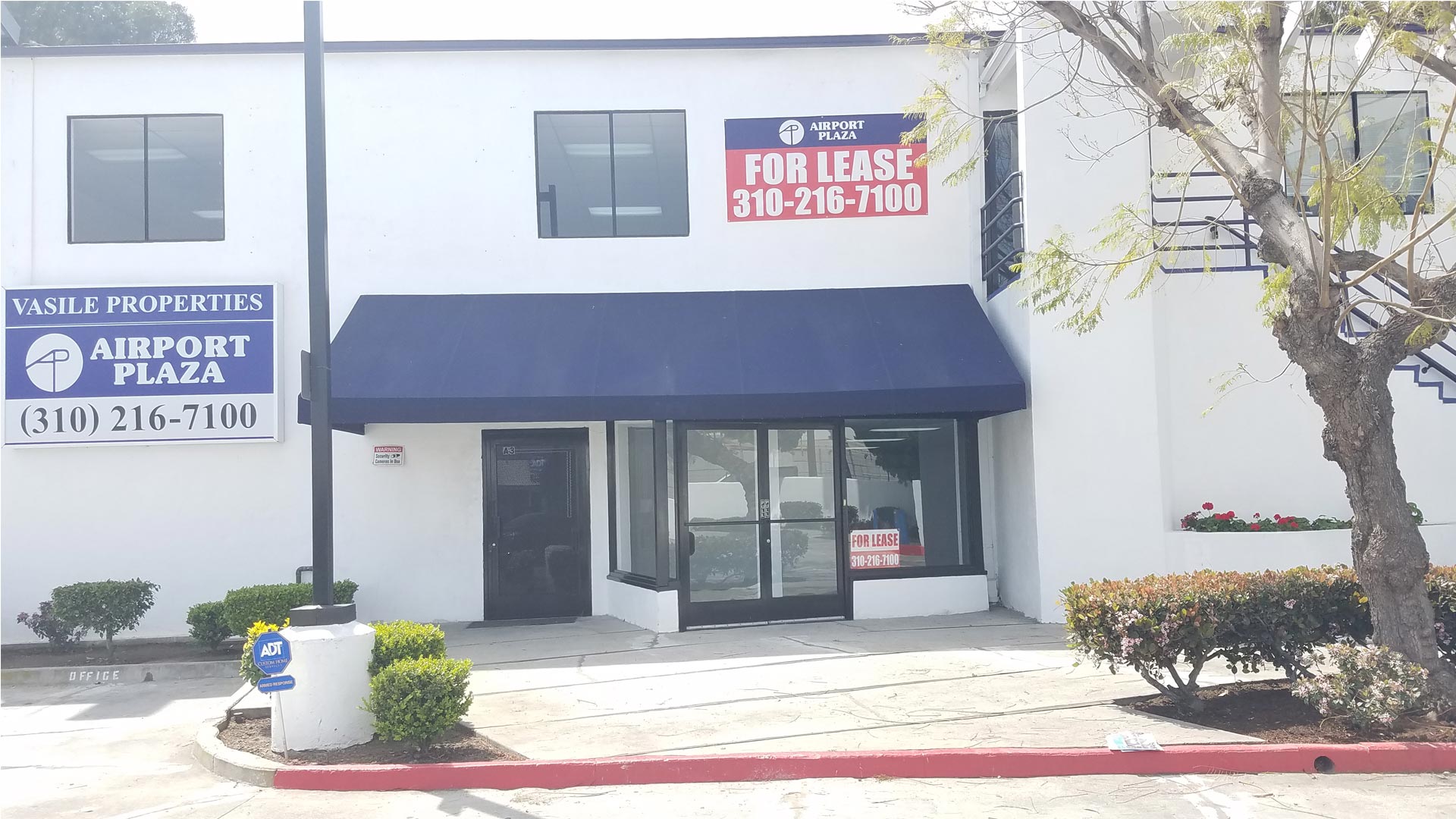 A building with a blue awning and for lease sign.
